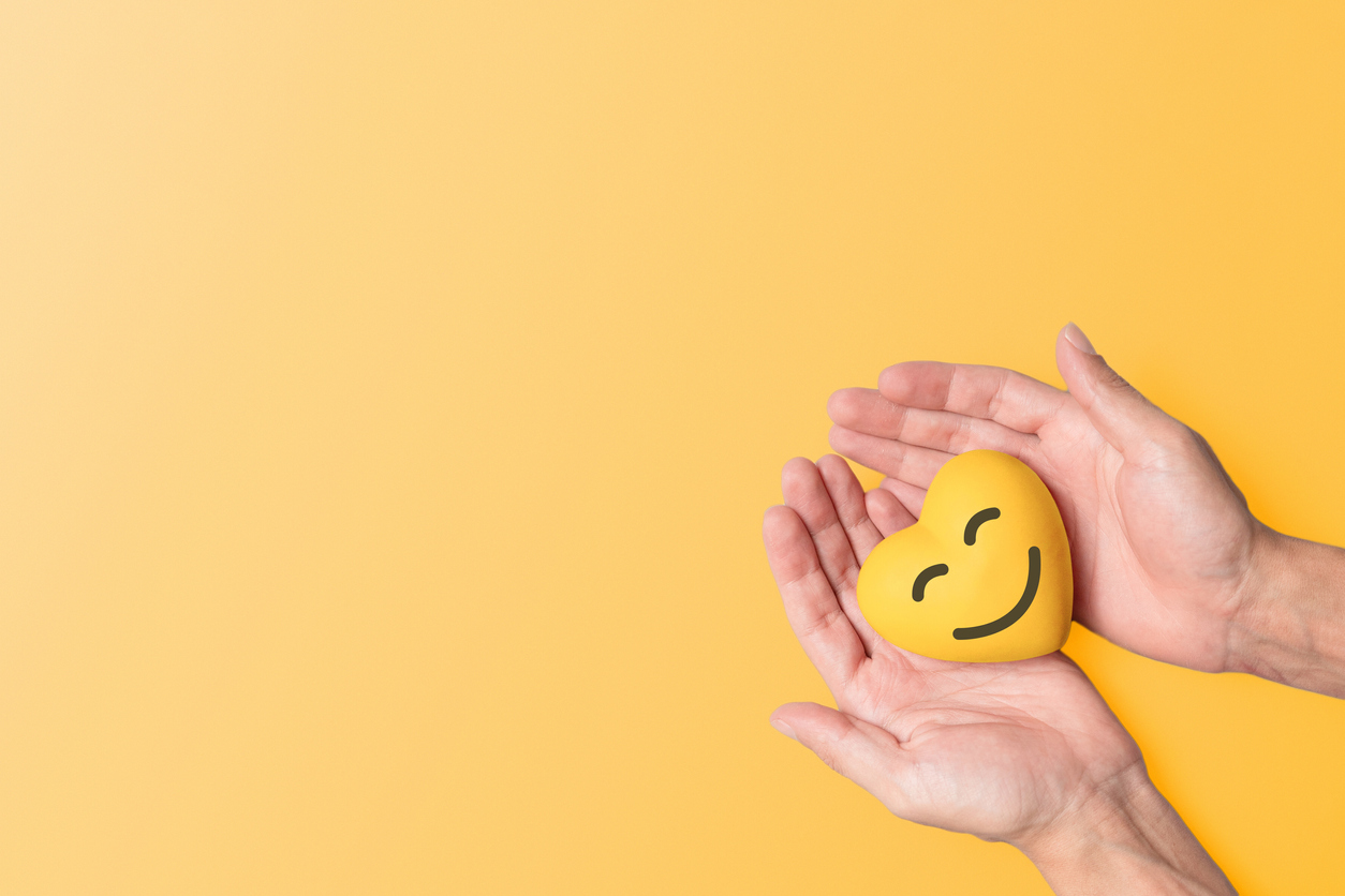 yellow heart with a smiley face in someones hands to represent positive thinking